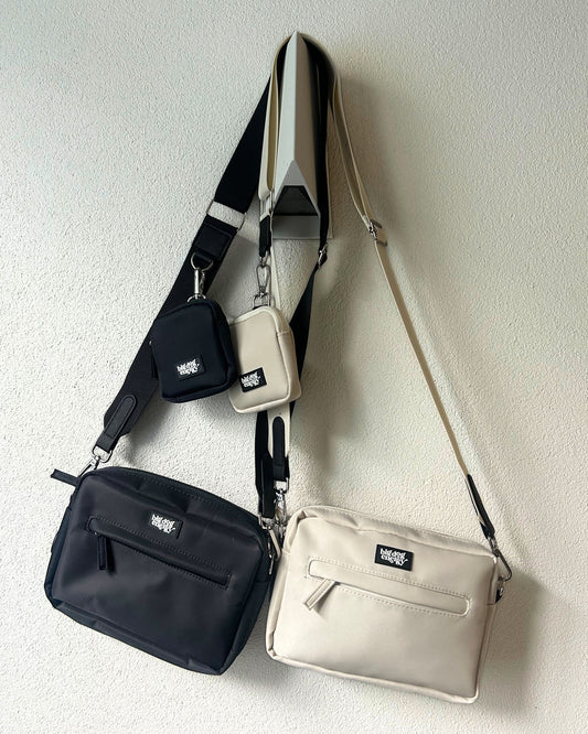 Two shoulder bags, one black and one beige, on a light cream background.